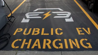 "Public EV Charging" sign with logo stenciled on black asphalt in parking lot.